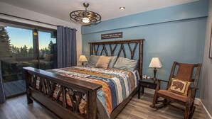 Een slaapkamer met een groot bed, een houten schommelstoel, een nachtkastje en een raam met gordijnen.