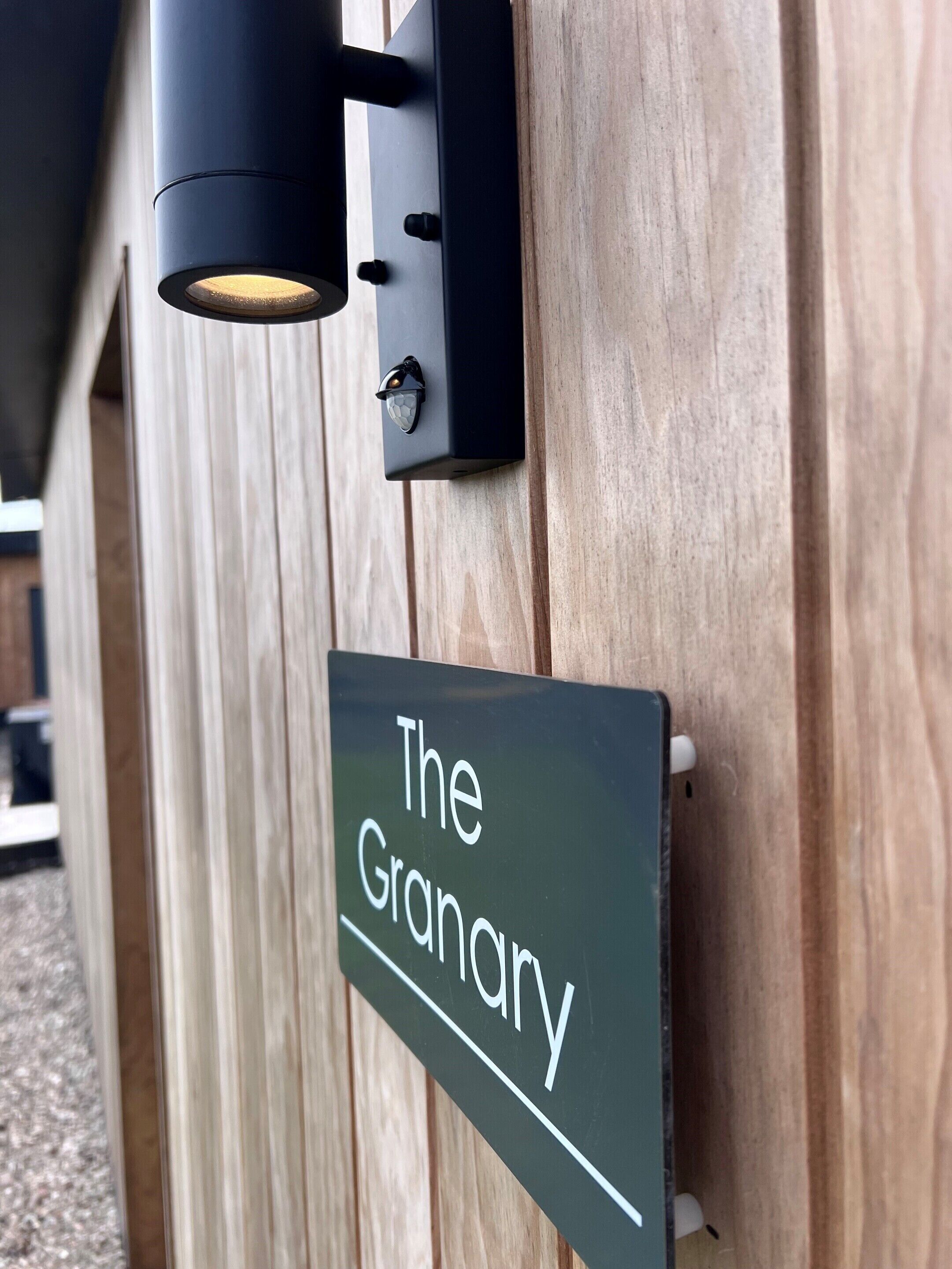Un mur en bois avec un luminaire noir et une enseigne sur laquelle on peut lire « The Granary ».