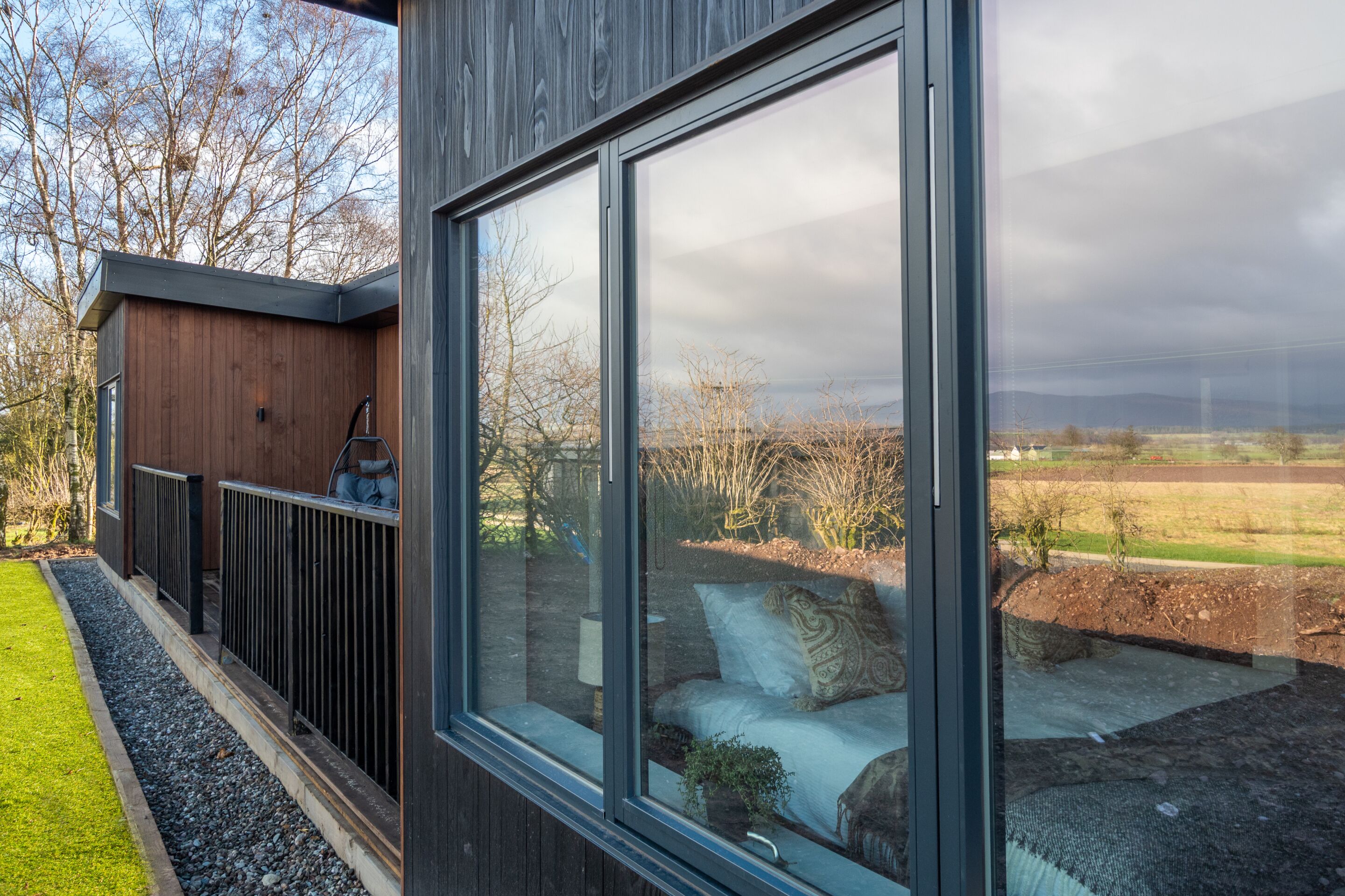 A modern cabin with a large window offering a view of a rural landscape.