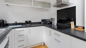 A modern kitchen with white cabinets, a black countertop, a built-in microwave, a toaster, and a coffee maker. - Church View (Exeter)