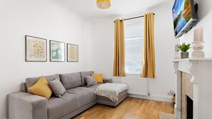 A modern living room with a grey sofa, mustard cushions, a fireplace, and framed artwork on the wall. - Church View (Exeter)