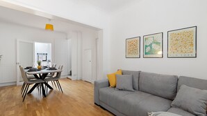 A modern living room with a grey sofa, a dining table with chairs, and three framed artworks on the wall. - Church View (Exeter)