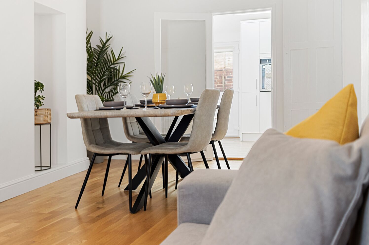 A modern dining area with a round table, grey upholstered chairs, and a yellow pillow on a grey sofa.
