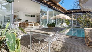 Um pátio moderno ao ar livre, com piscina, deck de madeira e móveis de metal branco.