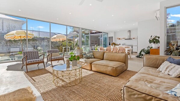 Relax in this open-plan living space with a sofa, chairs, dining table, and kitchen area, offering a view of the outdoors.