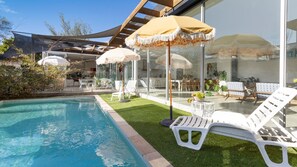 A swimming pool with white lounge chairs and umbrellas, surrounded by a well-maintained lawn and a glass-enclosed patio area. - POOLSIDE PARADISE - MOUNT ELIZA (Mount Eliza)