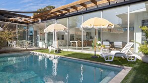 Uma área de piscina ao ar livre moderna, com paredes de vidro, espreguiçadeiras e guarda-sóis.