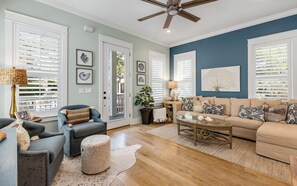A living room with a beige sofa, a blue armchair, a coffee table, and a ceiling fan.