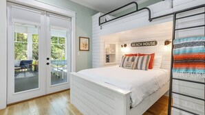Een slaapkamer met een stapelbed, een glazen deur die uitkomt op een terras, en een bordje aan de muur met de tekst 'BEACH HOUSE'.