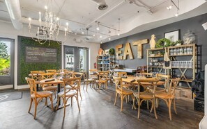 L’intérieur d’un restaurant avec des tables et des chaises en bois, un menu écrit à la craie et un grand panneau « À MANGER » accroché au mur.