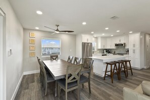 A modern kitchen with white cabinets, a central island, and a dining area with a wooden table and chairs.