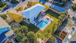 En vy från ovan av en bostadsfastighet med en swimmingpool, en inglasad uteplats och en inhägnad trädgård.