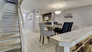 A dining area with a wooden table and chairs, a chandelier, and a staircase leading to another level.