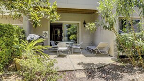 An outdoor patio with a table and chairs, surrounded by greenery and a building entrance.