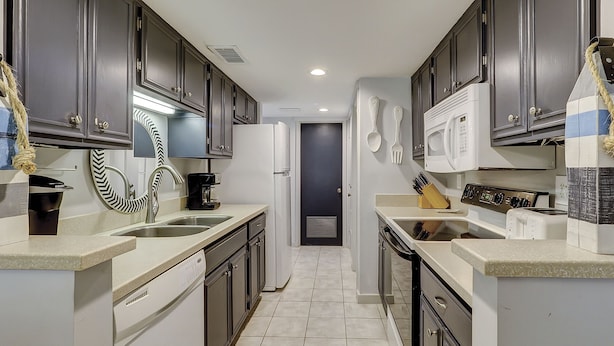 A narrow kitchen with dark cabinets, a white refrigerator, a microwave, and a coffee maker.