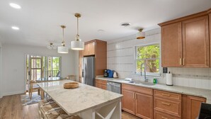 A modern kitchen with a large island, wooden cabinets, stainless steel appliances, and pendant lighting. - Home w/Dock, SUPs, Kayaks, Arcades, Ping-Pong (Leesville)