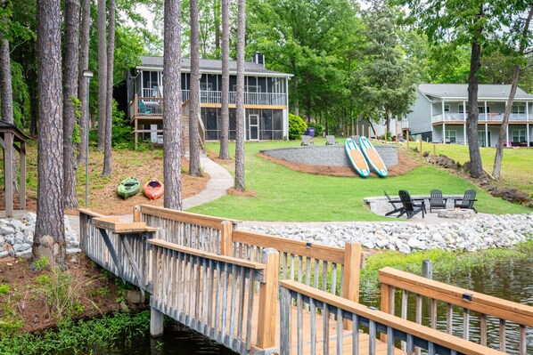 Escape to a serene lakeside retreat with a wooden bridge leading to a grassy area, surrounded by tall trees.
