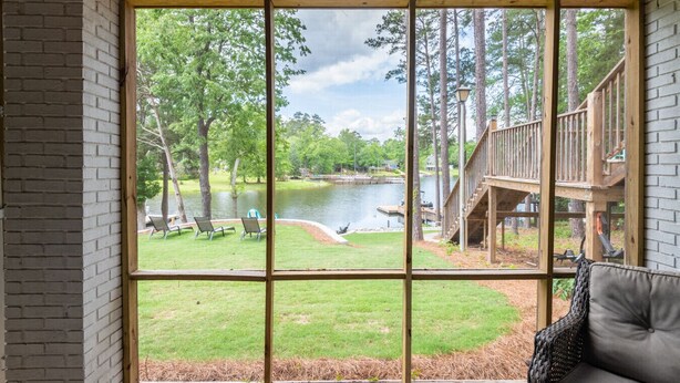 A room with a large window overlooking a pond, deck, and trees. - Home w/Dock, SUPs, Kayaks, Arcades, Ping-Pong (Leesville)