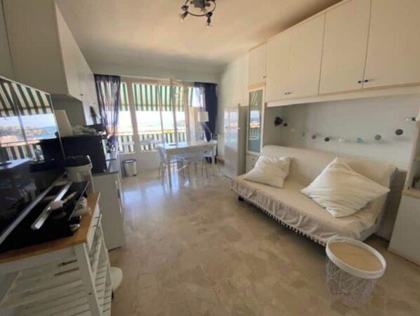 A modern kitchen with white cabinets, a dining area with a table and chairs, a sofa, and a view through large windows.