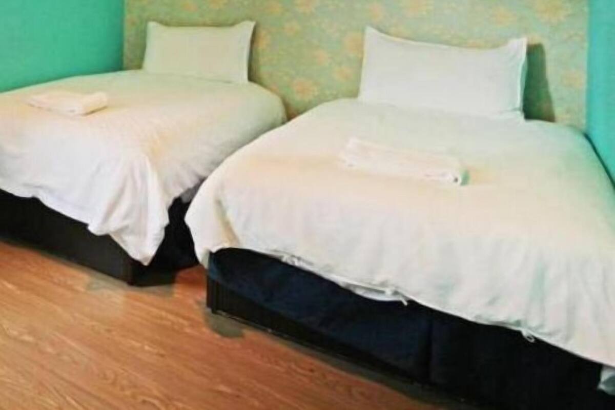 Una habitación con dos camas, cada una con ropa de cama y almohadas blancas, frente a una pared verde azulado con un estampado floral.
