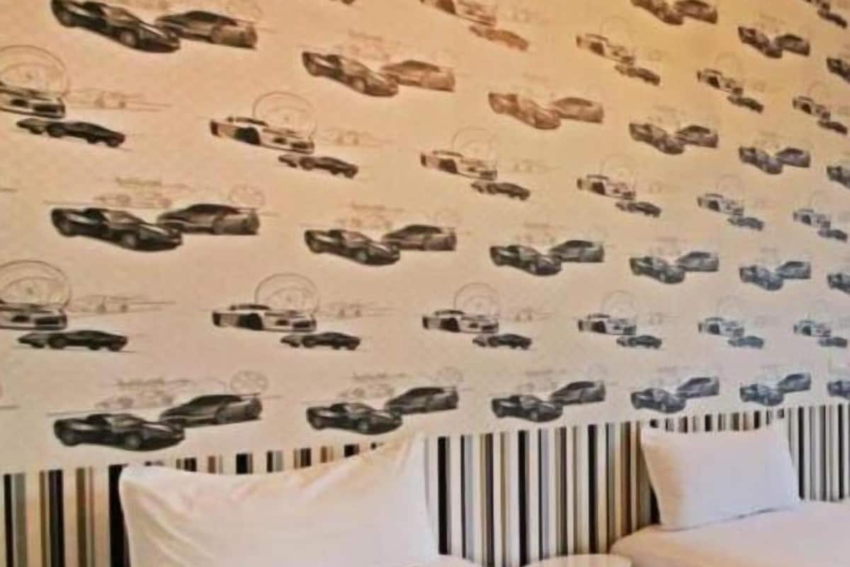 Habitación de hotel con dos camas, cabeceros a rayas y una pared decorada con un motivo repetido de ilustraciones de coches.