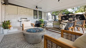 An outdoor patio with a stone wall, a fire pit, seating area, and a ceiling fan. - The Hansel-Modern 4 Bed, 3 Bath Bungalow, Hot Tub (Dallas)