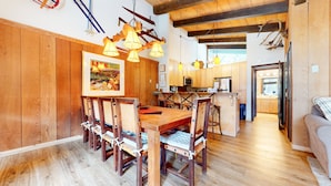 A wooden dining area with a long table and chairs, a kitchen in the background, and a cozy living space with a sofa. - Chateau Sans Nom #19 4 Bedroom Condo by RedAwning (Mammoth Lakes)