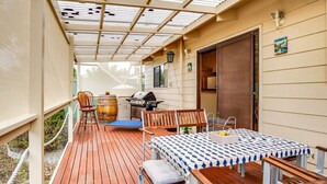 En overdækket terrasse med bord og stole, grill og træterrasse.