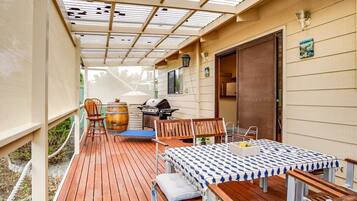 A covered outdoor patio with a table and chairs, a barbecue grill, and a wooden deck.