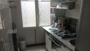 A compact kitchen with a window, a stove, a sink, and a trash bin. - Charmant Studio 42 M2 10 min de la Plage (Le Cannet)