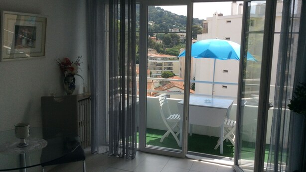 A balcony with a table and chairs, a glass door, and a view of buildings and greenery. - Charmant Studio 42 M2 10 min de la Plage (Le Cannet)