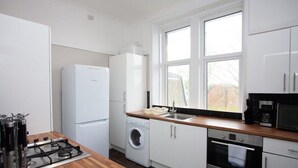 A modern kitchen with white cabinets, a built-in washing machine, a gas stove, and a large window providing natural light.