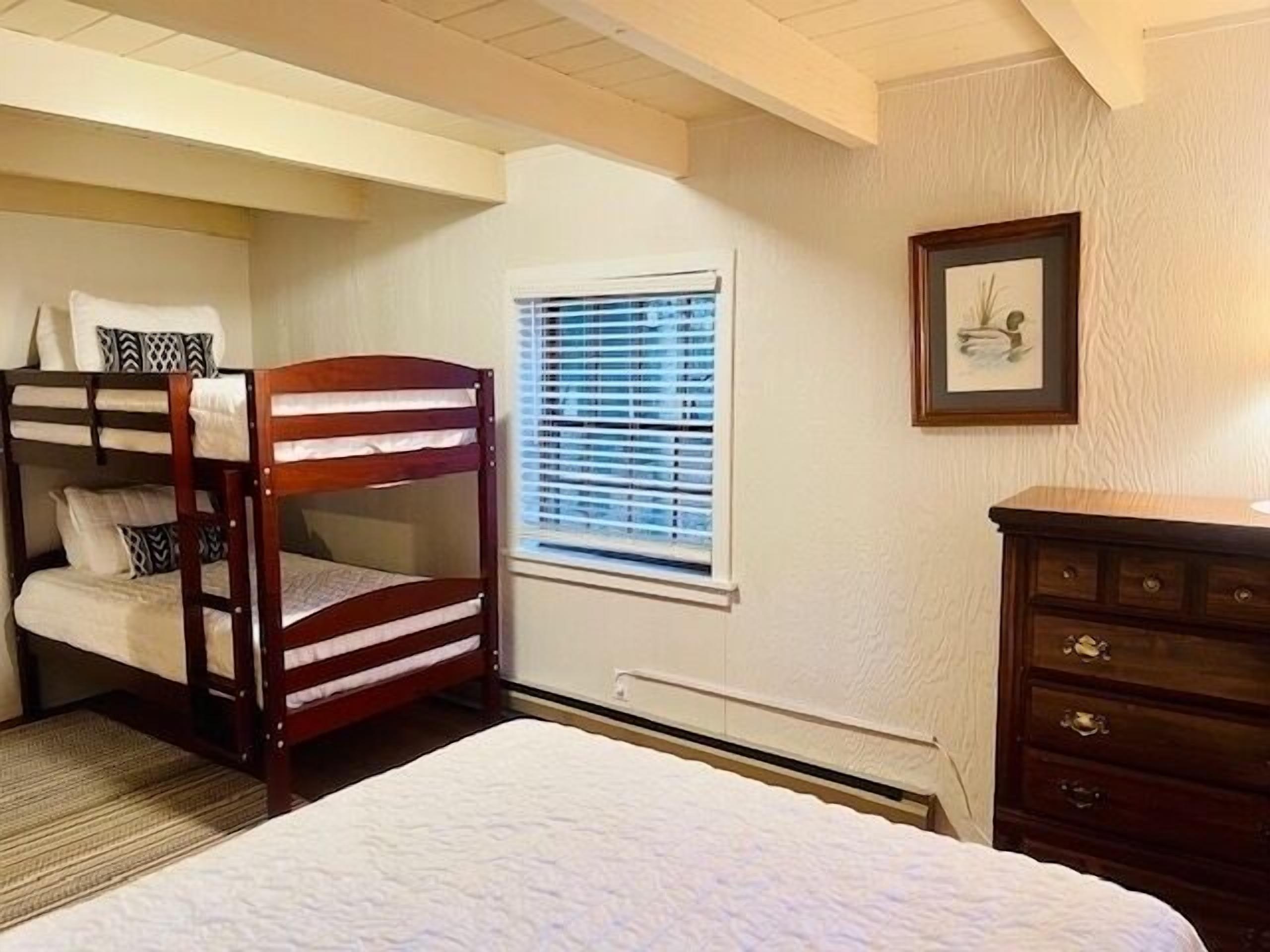 A bedroom with bunk beds, a window with blinds, a dresser, and a framed picture on the wall.