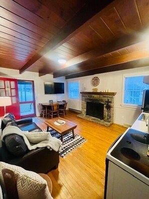 A cozy living room with a fireplace, wooden floors, a dining area, and a kitchen.