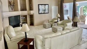 A spacious living room with a large white sofa, two armchairs, a TV, and a ceiling fan. - Family Canal House/ Heated Pool, Kayaks, BBQ, Lift (Cape Coral)
