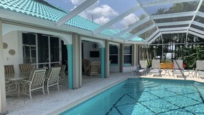 A swimming pool with clear blue water, surrounded by lounge chairs and a covered patio area. - Family Canal House/ Heated Pool, Kayaks, BBQ, Lift (Cape Coral)