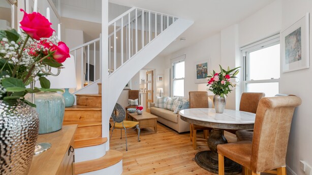 A spacious living area with a wooden staircase, a round dining table, and comfortable seating. - The Nestle House (Winchester)
