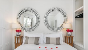 A neatly made bed with rose petals, two round mirrors with crystal frames, and two bedside tables with lamps and vases of red roses. - The Nestle House (Winchester)