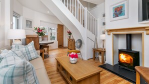 A spacious living room with a wooden floor, a sofa, a coffee table, a fireplace, and a staircase. - The Nestle House (Winchester)