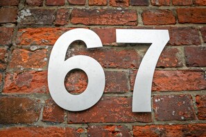 Um número '67' grande e metálico fixado numa parede de tijolos.