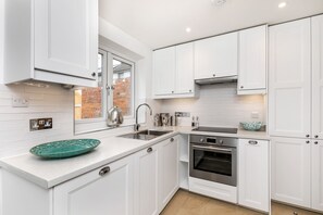 Uma cozinha moderna com armários brancos, forno de aço inoxidável e uma janela ampla.