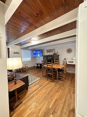 A dining area with a wooden table and chairs, a TV mounted on the wall, and a fireplace.