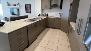 A modern kitchen with grey cabinets, a stainless steel sink, and a tiled floor.