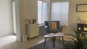 A living room with a grey sofa, a small table, a grey rug, and a potted plant.