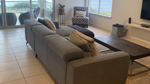 A modern living room with a grey sectional sofa, a small round table, and a TV mounted on the wall.