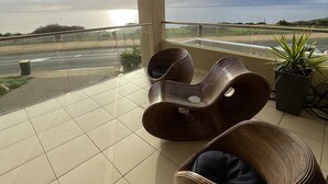 A balcony with wicker chairs, a potted plant, and a view of the sea.
