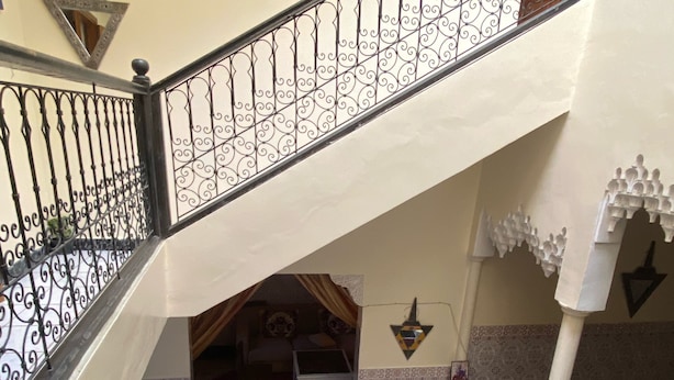 Comedor con piso a cuadros, una mesa dispuesta para cuatro comensales y una escalera con barandilla decorada.