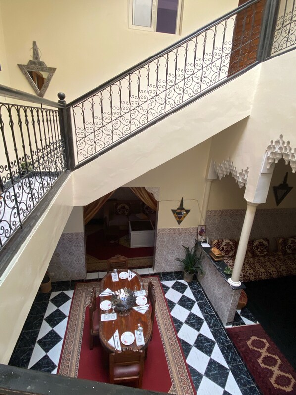 Un coin repas avec un sol à carreaux, une table à manger dressée pour quatre personnes et un escalier agrémenté de rampes décoratives.