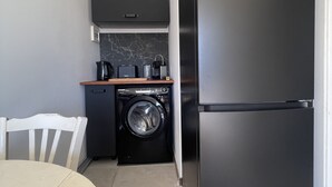 A compact kitchen with a black Haier refrigerator, a washing machine, and a coffee maker on a wooden countertop. - Cap Corse, Sisco. Apartment in stone village house with sea view  (Sisco)