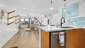 A modern kitchen with a central island, a built-in dishwasher, and a view of the living area.